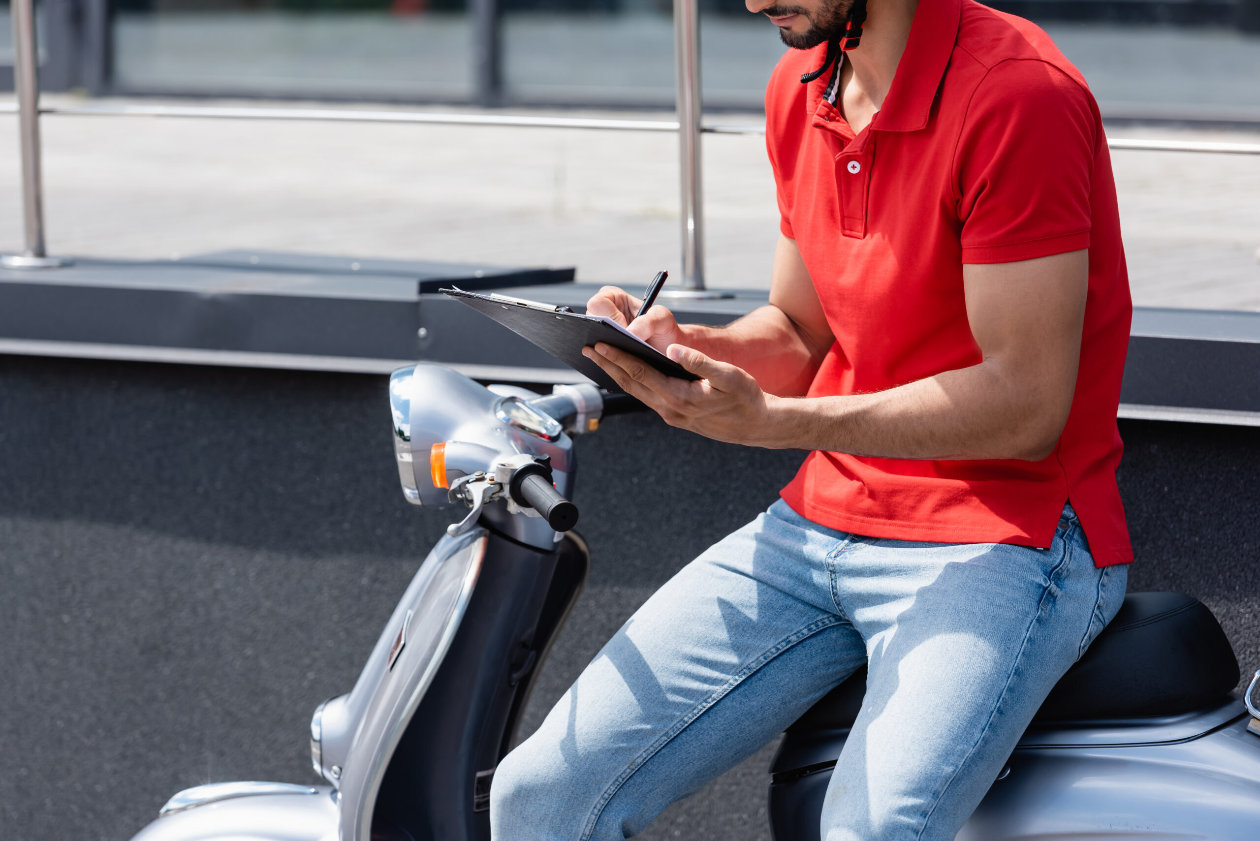 Cropped view of courier writing on clipboard on scooter on urban street