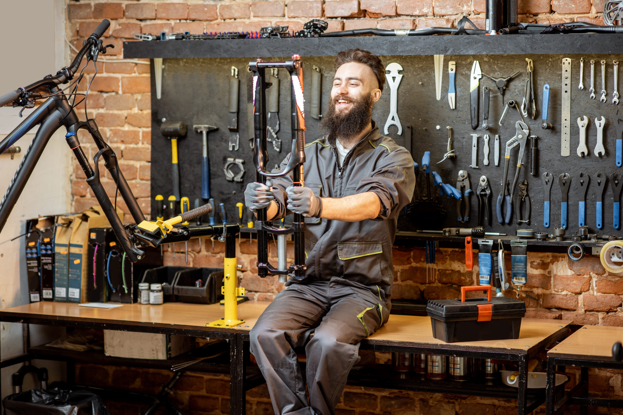 Portrait of a handsome repairman in workwear sitting with bicycle fork on the table in the bicycle workshop